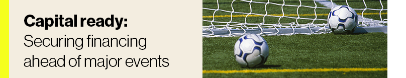Two soccer balls in front of a net on the playing field.